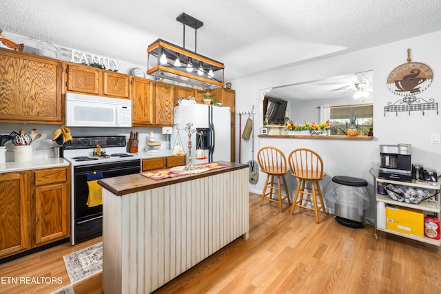 kitchen featuring white appliances, light wood-type flooring, a textured ceiling, and pendant lighting