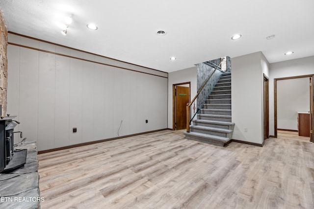 unfurnished living room featuring wood walls, a wood stove, and light wood-type flooring