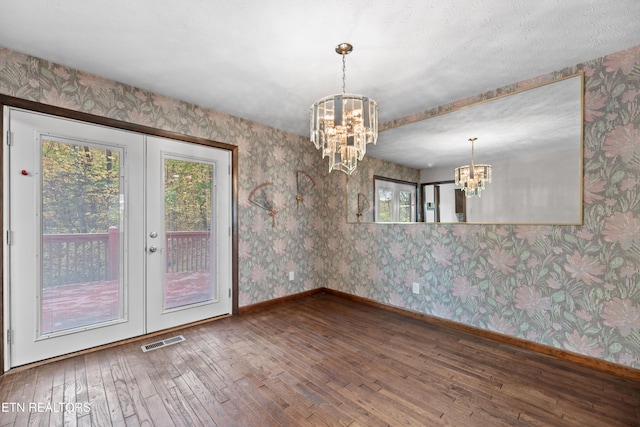 unfurnished dining area with french doors, a notable chandelier, and hardwood / wood-style flooring