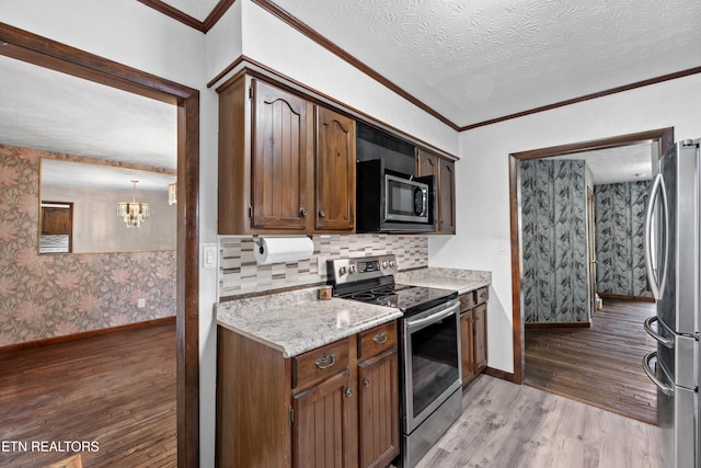 kitchen featuring crown molding, appliances with stainless steel finishes, a textured ceiling, and light wood-type flooring