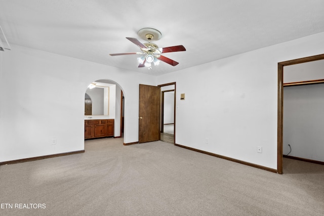 unfurnished bedroom featuring a closet, ceiling fan, light carpet, and ensuite bath