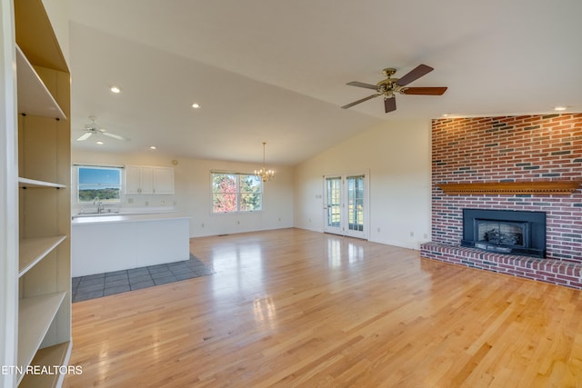 unfurnished living room with sink, ceiling fan with notable chandelier, a fireplace, vaulted ceiling, and light hardwood / wood-style flooring