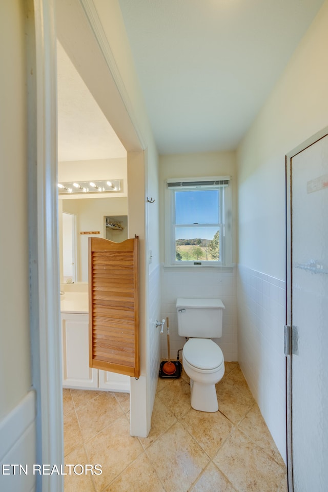 bathroom with toilet, vanity, tile patterned floors, and tile walls