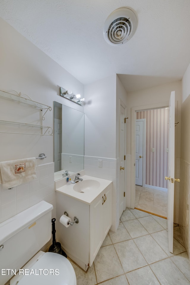 bathroom featuring toilet, tile patterned flooring, vanity, tile walls, and a textured ceiling