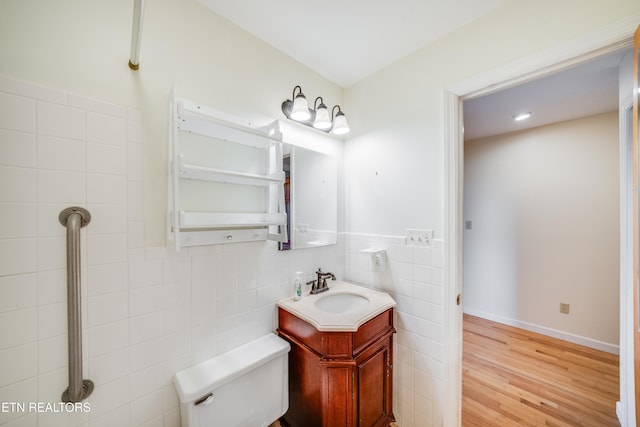 bathroom with toilet, hardwood / wood-style floors, vanity, and tile walls