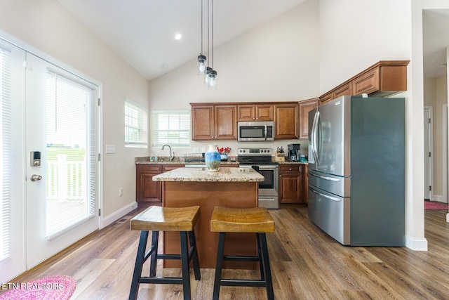 kitchen with appliances with stainless steel finishes, decorative light fixtures, a kitchen island, and wood-type flooring