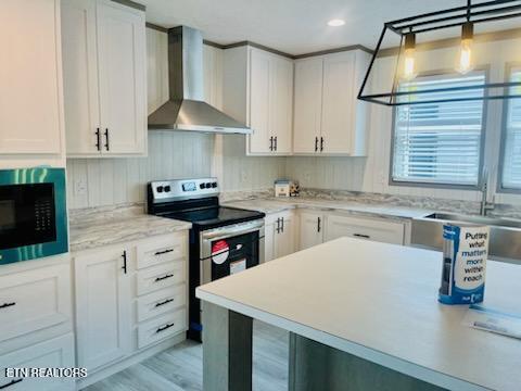 kitchen featuring wall chimney exhaust hood, stainless steel electric range, decorative light fixtures, light wood-type flooring, and white cabinetry