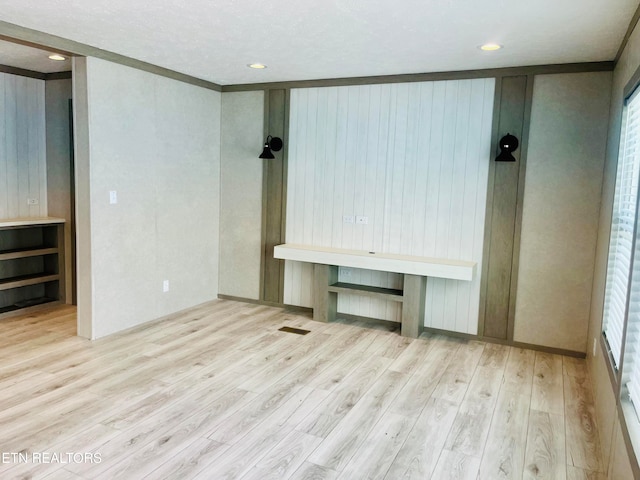 unfurnished bedroom featuring light hardwood / wood-style floors, crown molding, and wood walls