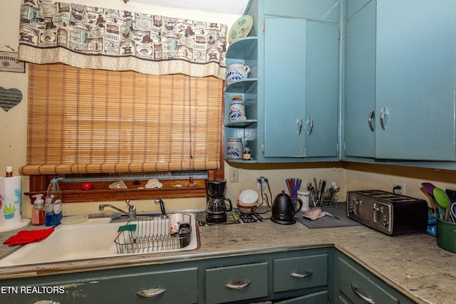 kitchen featuring a sink, open shelves, blue cabinetry, and light countertops