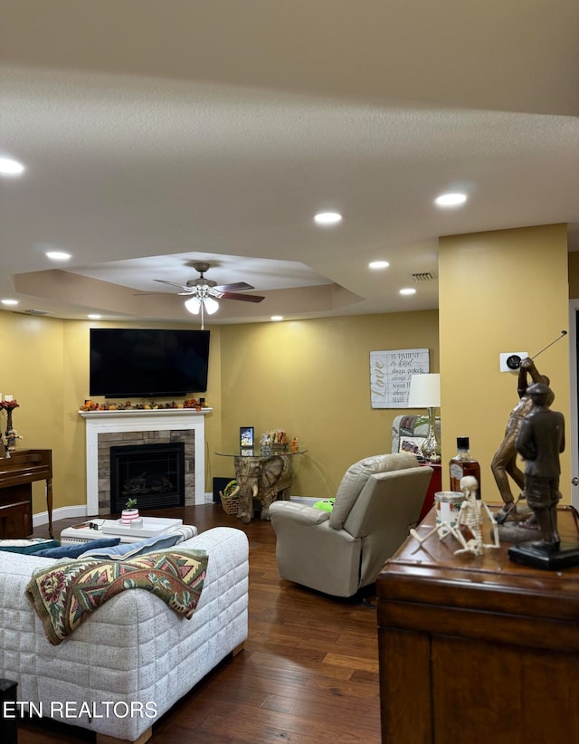 living room featuring dark wood-type flooring, ceiling fan, a tray ceiling, and a tile fireplace