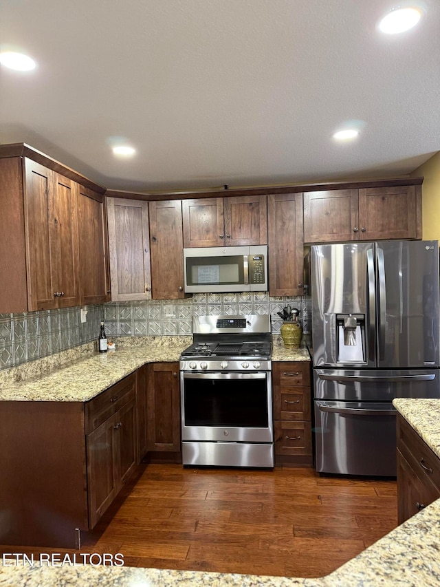 kitchen with decorative backsplash, light stone countertops, stainless steel appliances, and dark hardwood / wood-style flooring