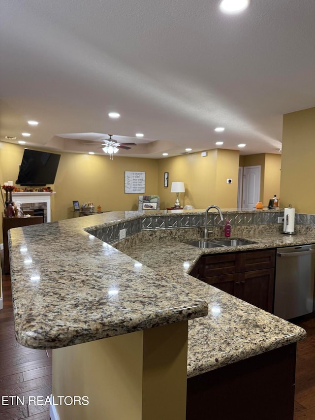 kitchen featuring a tiled fireplace, sink, dark hardwood / wood-style flooring, stainless steel dishwasher, and ceiling fan