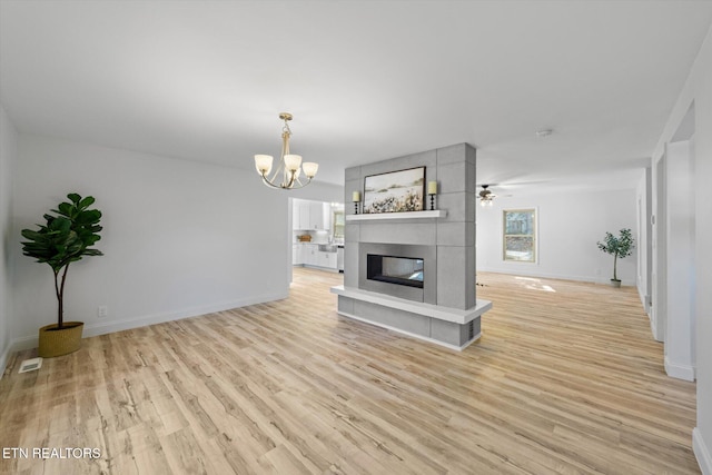 unfurnished living room featuring ceiling fan with notable chandelier, light hardwood / wood-style floors, and a fireplace