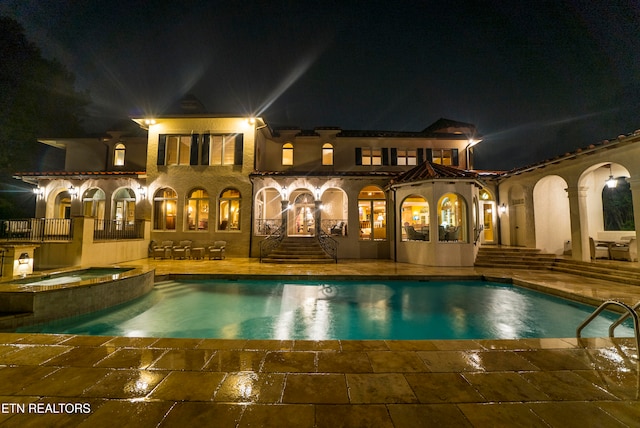 pool at twilight featuring an in ground hot tub and a patio area