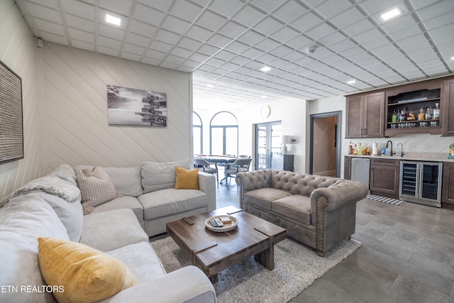 living room with wet bar, a paneled ceiling, wooden walls, and beverage cooler