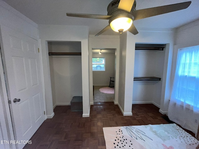 unfurnished bedroom featuring multiple windows, dark parquet floors, two closets, and ceiling fan