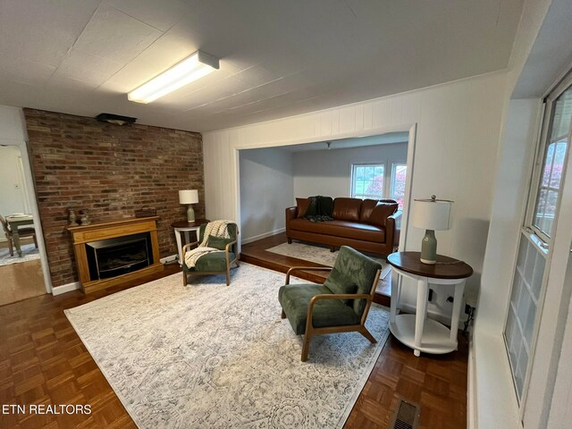 living room featuring dark parquet flooring, a fireplace, and brick wall