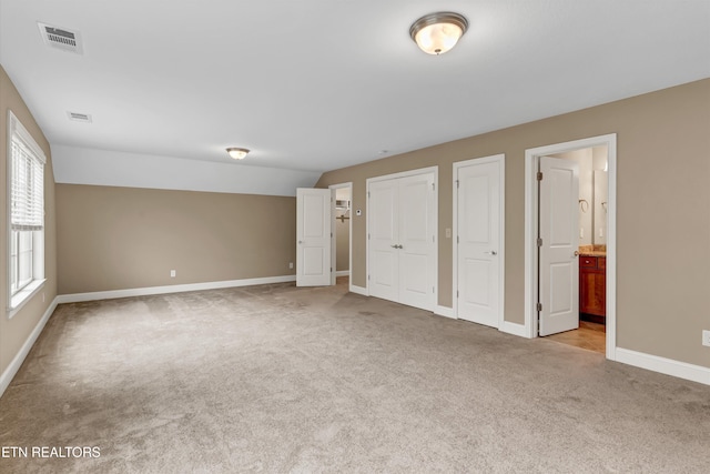 unfurnished bedroom with multiple closets, light colored carpet, and connected bathroom