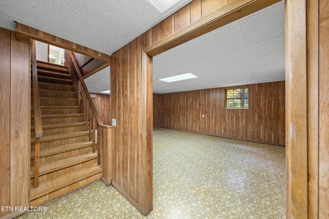 basement with a drop ceiling and wooden walls