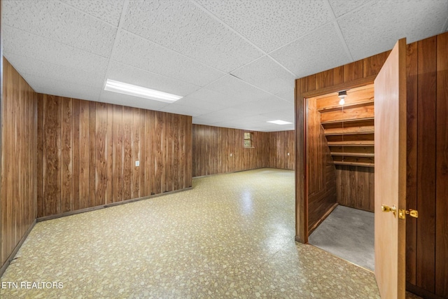 basement with wood walls and a paneled ceiling