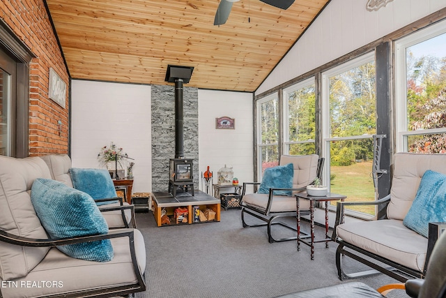 sunroom / solarium with vaulted ceiling, ceiling fan, a wood stove, and wooden ceiling