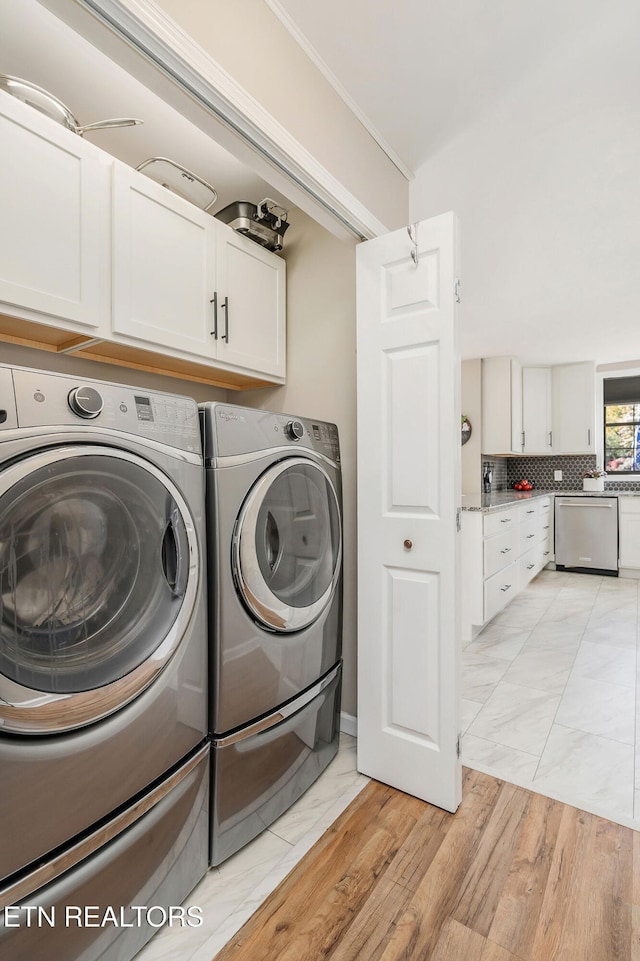 laundry room with crown molding, washing machine and dryer, light hardwood / wood-style flooring, and cabinets