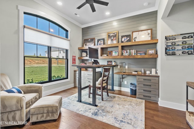 office area with ceiling fan, wood walls, ornamental molding, and dark wood-type flooring