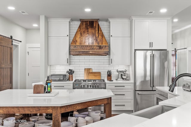 kitchen with custom exhaust hood, a barn door, white cabinetry, and high end fridge