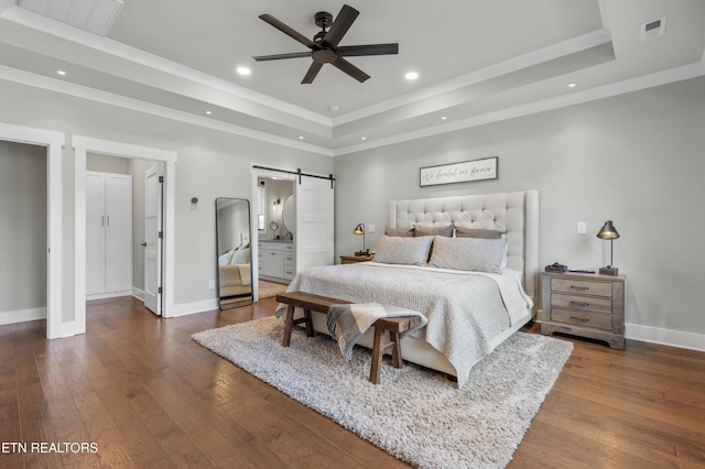 bedroom with ensuite bath, ceiling fan, a barn door, hardwood / wood-style floors, and a tray ceiling