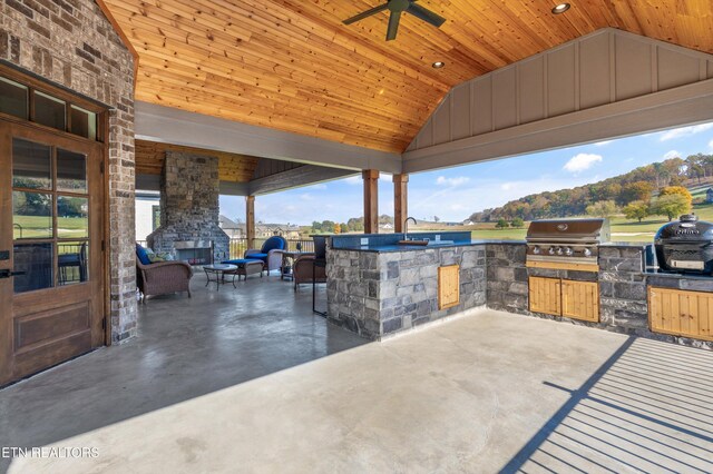 view of patio featuring an outdoor kitchen, an outdoor stone fireplace, sink, a mountain view, and a grill