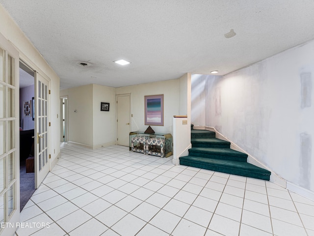 basement with french doors, a textured ceiling, and light tile patterned floors