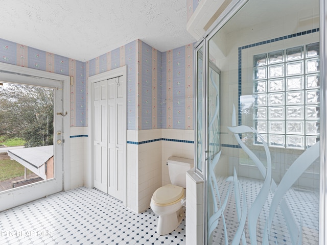 bathroom with a textured ceiling, toilet, tile walls, and a wealth of natural light