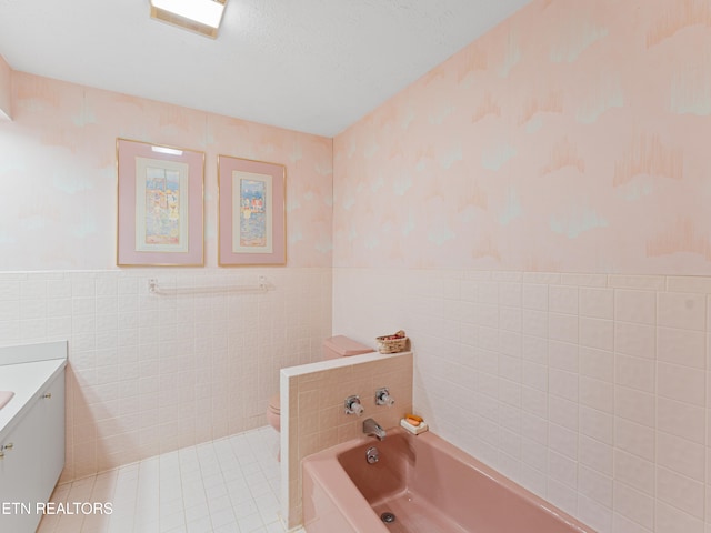 bathroom with a tub, vanity, tile walls, and toilet