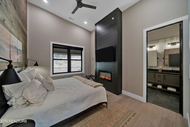 bedroom featuring ceiling fan, connected bathroom, light wood-type flooring, a fireplace, and sink