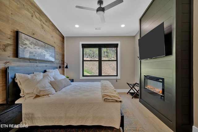 bedroom with wooden walls, light hardwood / wood-style flooring, and ceiling fan