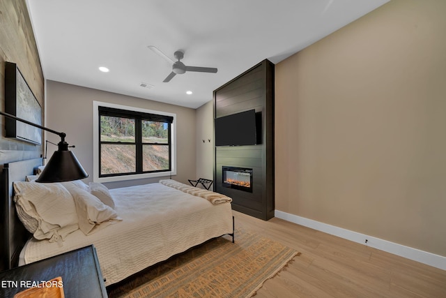 bedroom featuring light hardwood / wood-style flooring, a fireplace, and ceiling fan