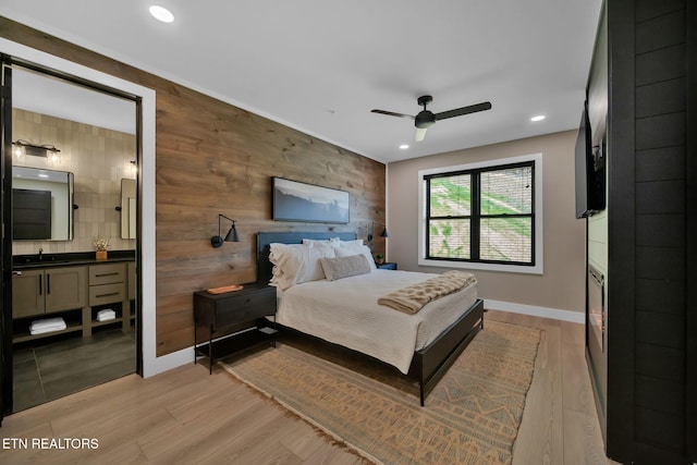 bedroom featuring wood walls, sink, ceiling fan, connected bathroom, and light hardwood / wood-style flooring