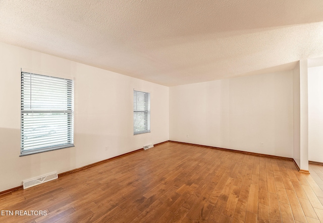 spare room featuring a wealth of natural light, wood-type flooring, and a textured ceiling