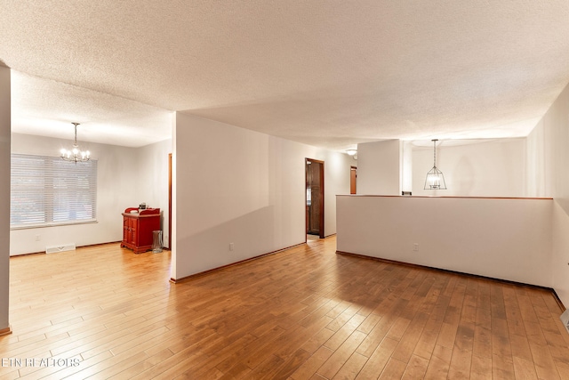 empty room featuring hardwood / wood-style floors, a textured ceiling, and an inviting chandelier