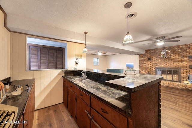 kitchen with sink, brick wall, a textured ceiling, a brick fireplace, and light wood-type flooring