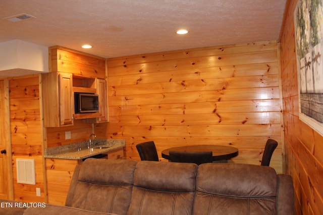 living room featuring a textured ceiling, sink, and wooden walls