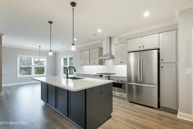 kitchen with wall chimney exhaust hood, sink, high quality appliances, light hardwood / wood-style floors, and hanging light fixtures