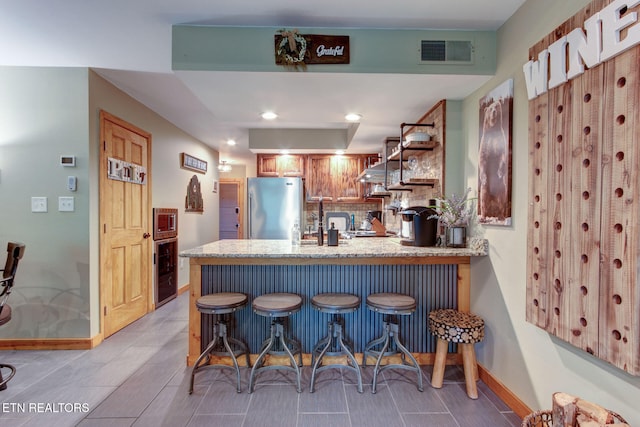 kitchen with tasteful backsplash, kitchen peninsula, a kitchen breakfast bar, and stainless steel fridge