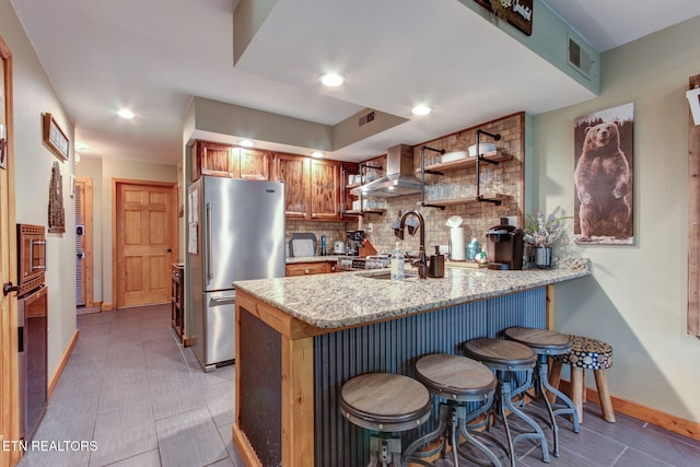 kitchen featuring wall chimney range hood, kitchen peninsula, tasteful backsplash, and stainless steel appliances