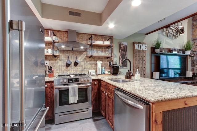 kitchen with light stone countertops, wall chimney range hood, sink, kitchen peninsula, and stainless steel appliances