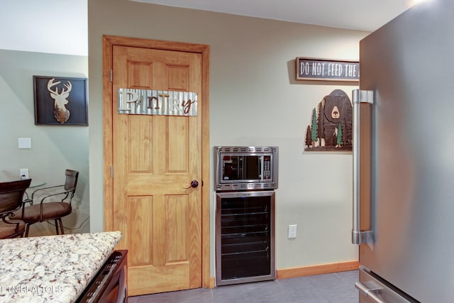 kitchen featuring light stone countertops, stainless steel fridge, light tile patterned flooring, and beverage cooler