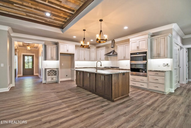 kitchen featuring dark hardwood / wood-style floors, backsplash, a center island with sink, appliances with stainless steel finishes, and light stone counters