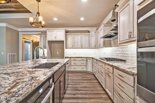 kitchen featuring dark wood finished floors, a barn door, light stone counters, appliances with stainless steel finishes, and a sink