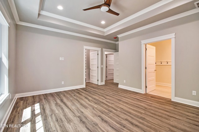 unfurnished bedroom featuring a raised ceiling, hardwood / wood-style floors, ceiling fan, connected bathroom, and crown molding