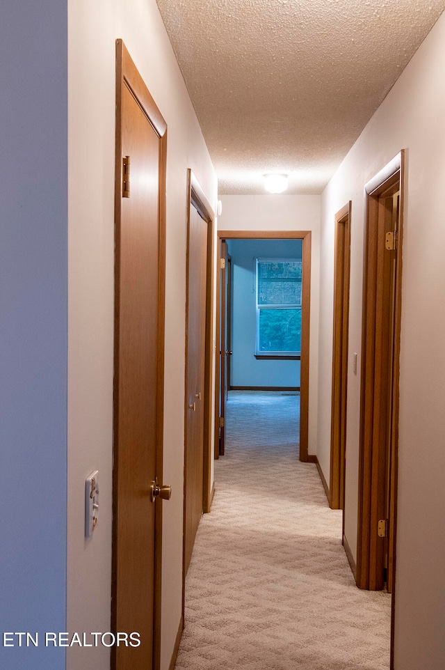 corridor featuring a textured ceiling and light carpet